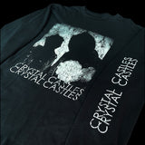 Angular close up of the front of a Black t-shirt with 'Crystal Castles' graphic design and 'crystal castles' on sleeve on a black background