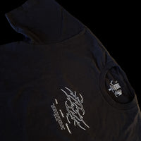 Angled view of black t-shirt with neotribal “Fallen Angel” flame logo and Latin microtext reading “Ave Dominum Inferni” – gothic streetwear